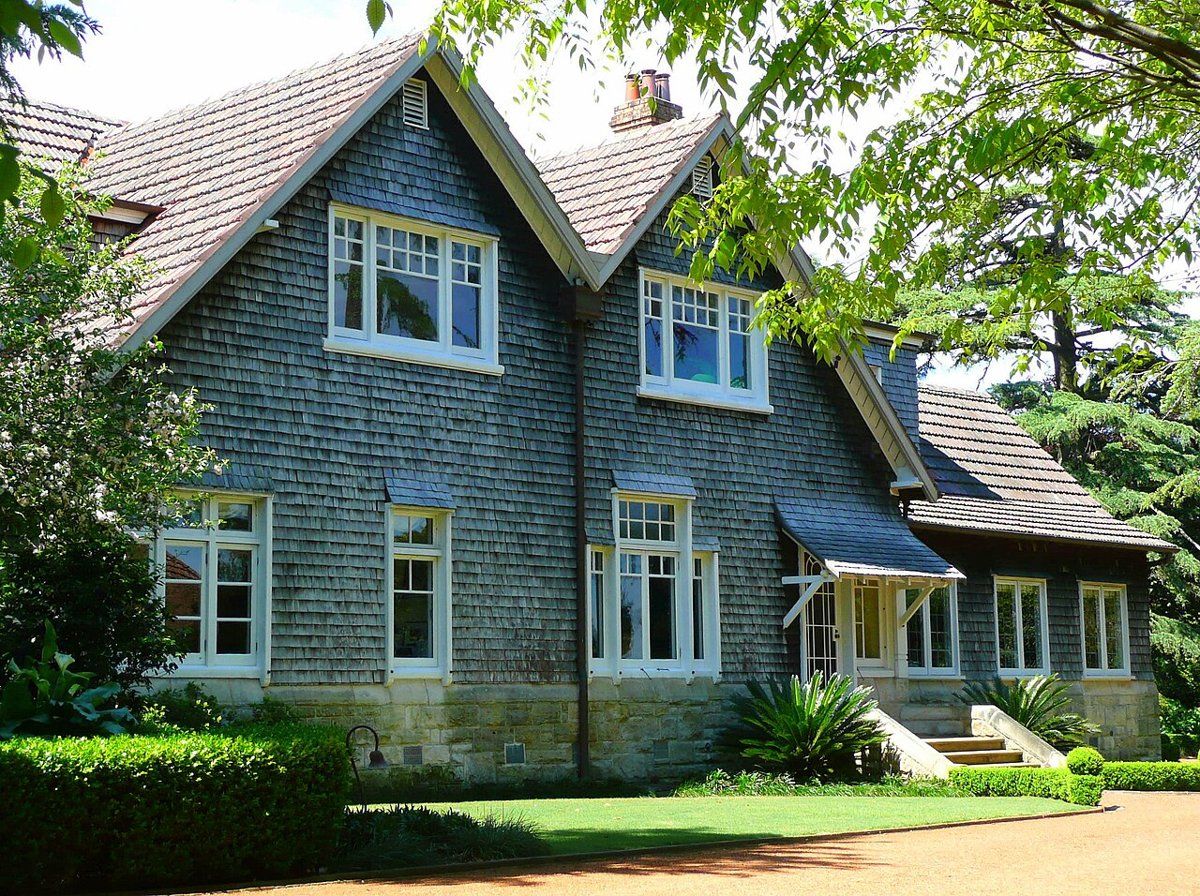 Pibrac, a large two-storey house with grey shingled walls on a sandstone base, a lawn and clipped hedges, in Warrawee