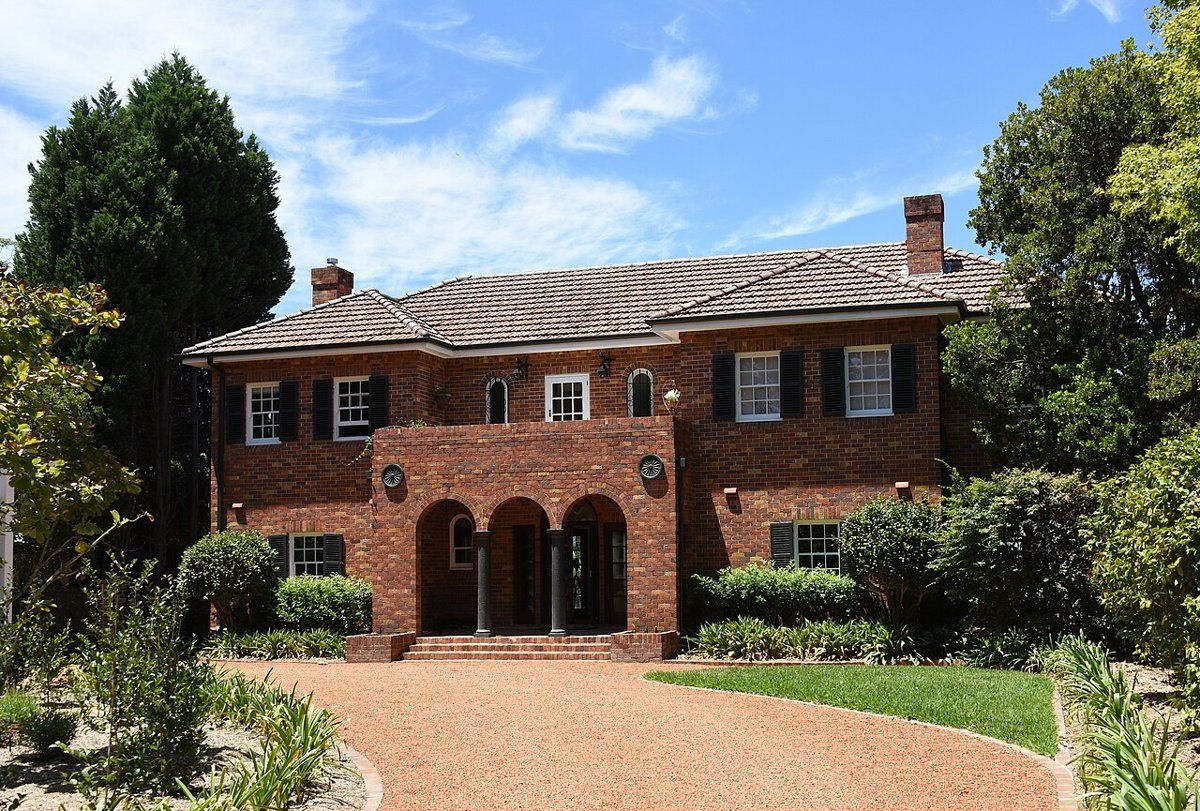 A two-storey red-brick house in Pymble with a gravel forecourt, hedges and established trees