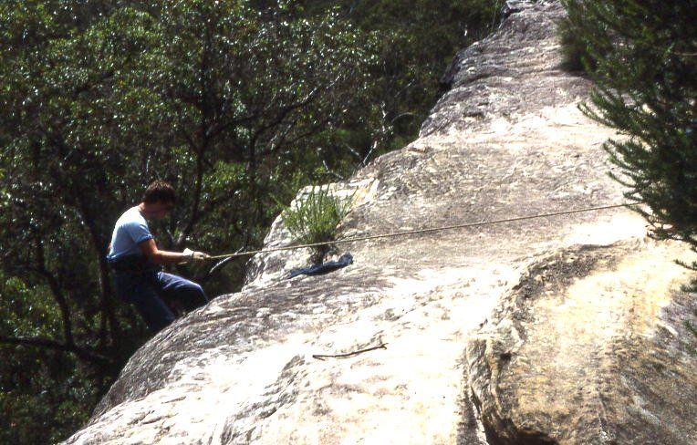 A climber abseiling down a sandstone cliff among bush near Cliff Avenue, North Wahroonga