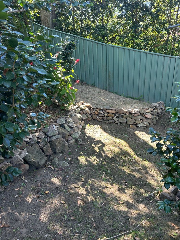 A curved sandstone dry stone wall holding a level garden bed